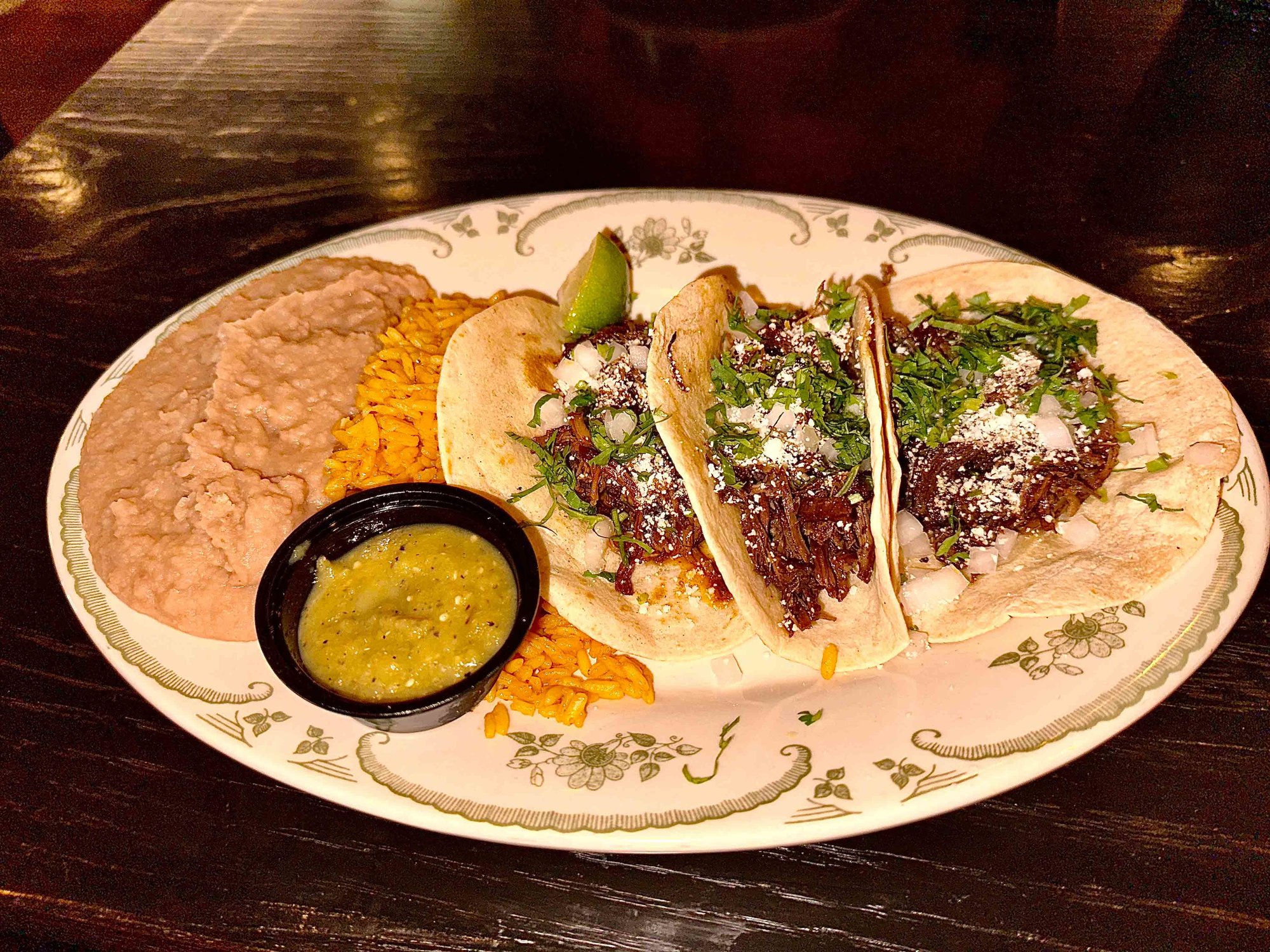 three barbacoa tacos with rice and beans on a plate